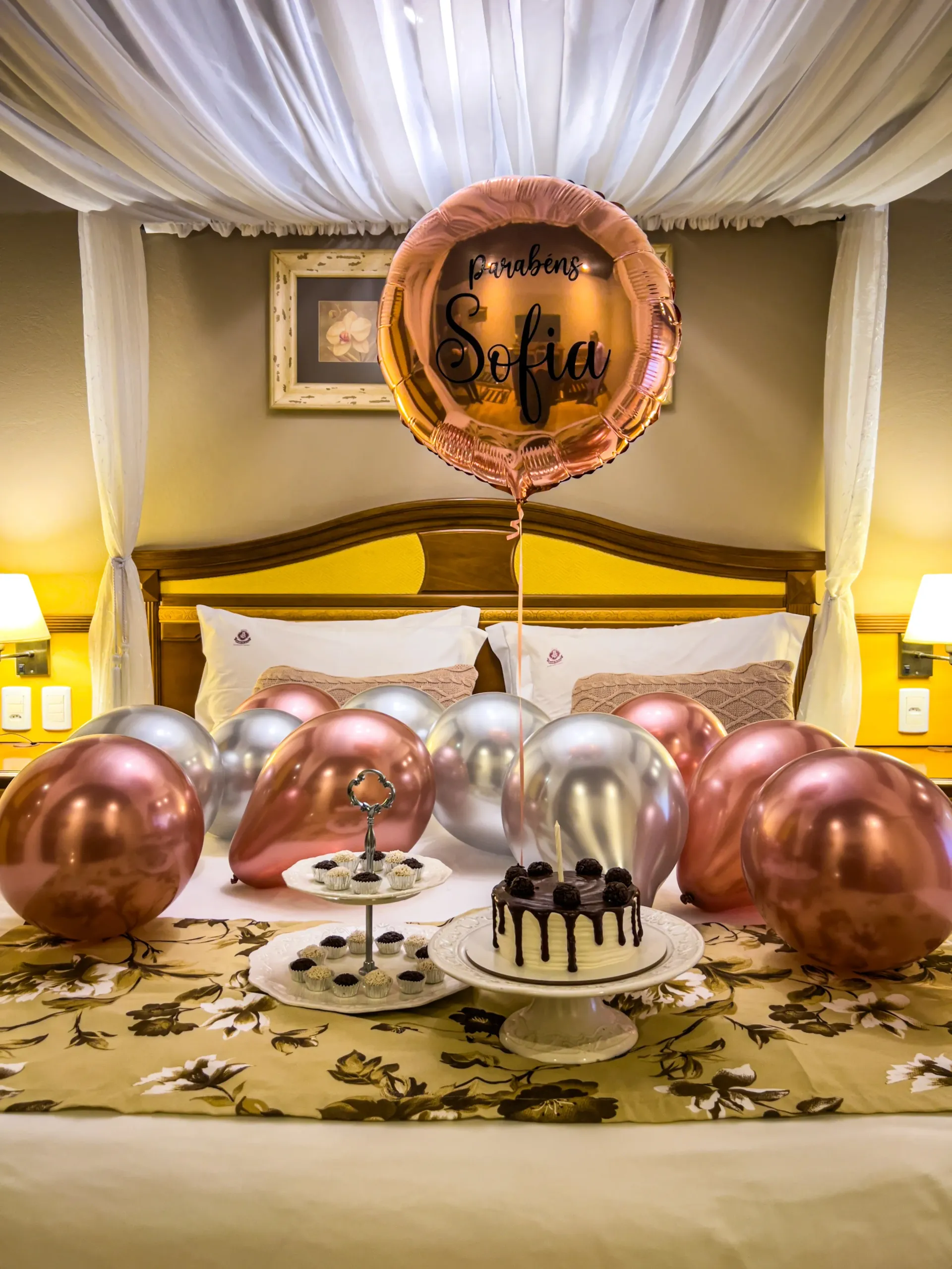 Decoração do pacote Felicitá com bolo, docinhos e balões sobre a cama, no hotel para aniversário.