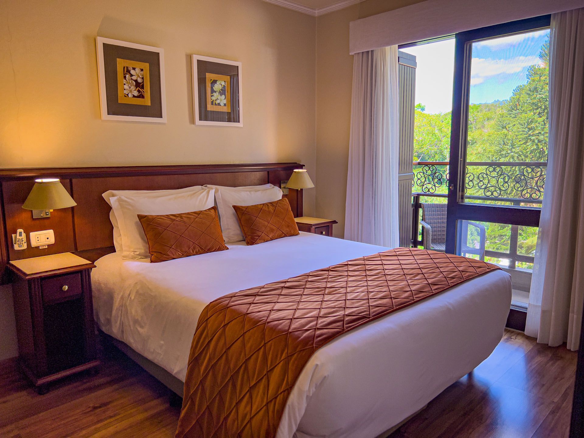 Quarto aconchegante com cama, iluminação quente e portas de varanda que se abrem para uma vista verdejante da montanha.