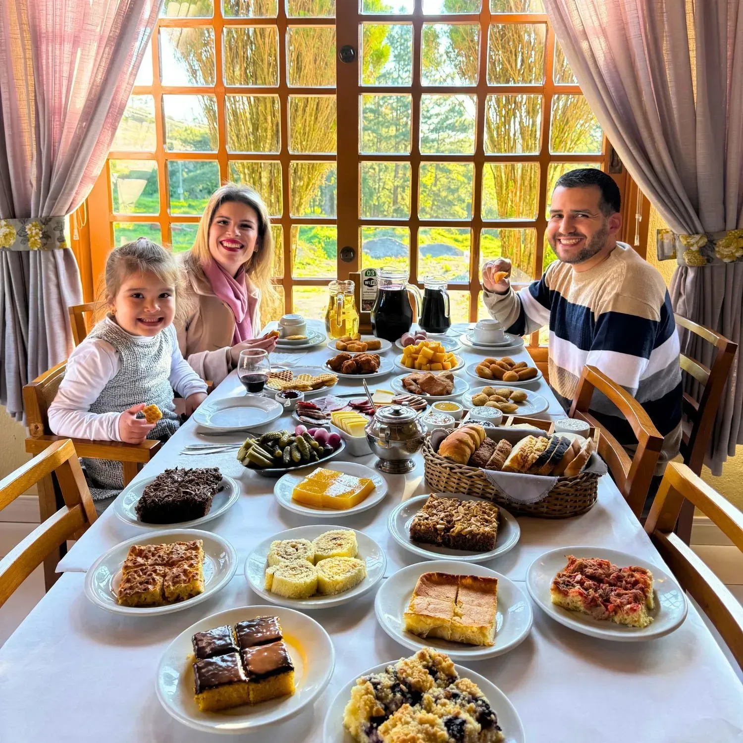 Família reunida à mesa farta do Gramado Café Colonial, com cucas, bolos, pães, frios e geleias servidos no buffet.