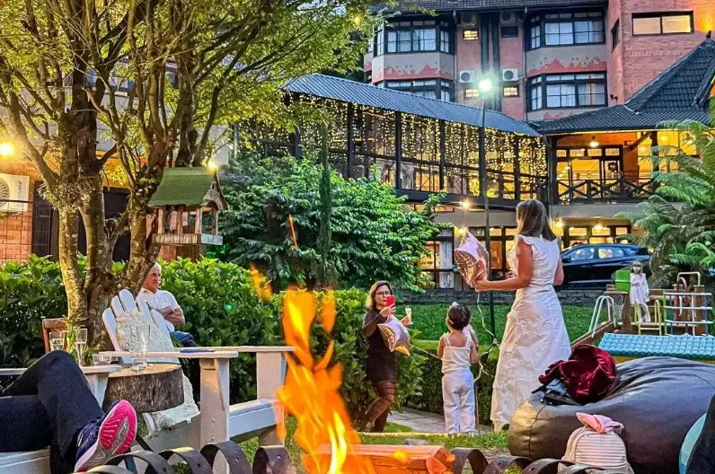 Área externa e iluminada do Hotel Recanto da Serra ao anoitecer, com hóspedes relaxando ao redor de