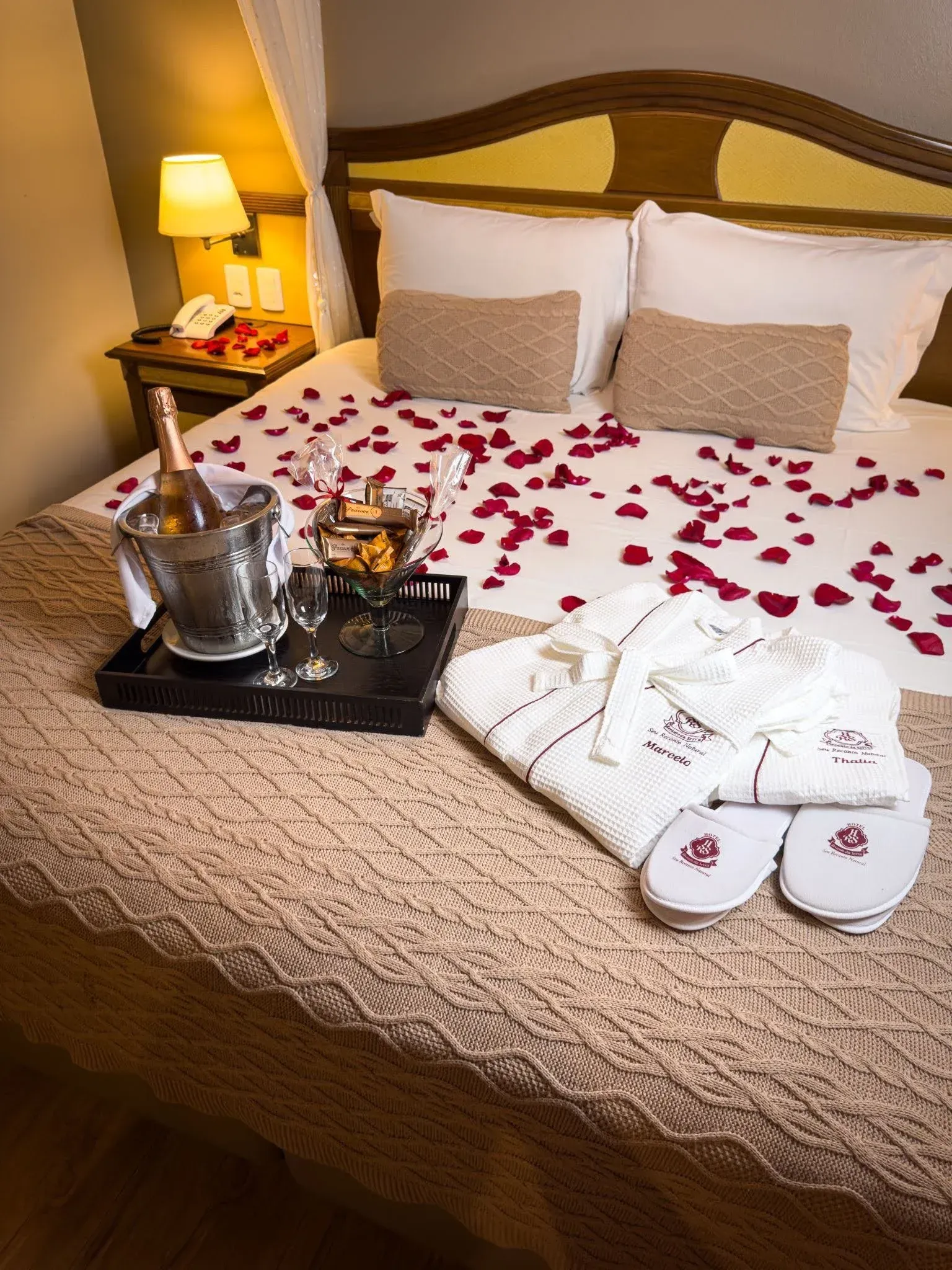 Quarto de hotel em Gramado com decoração romântica de pétalas de rosas na cama, espumante no balde d