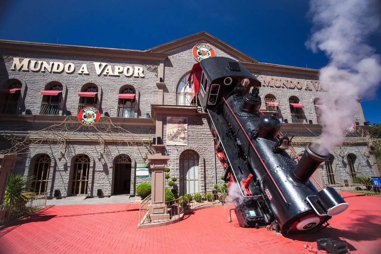 Fachada de pedra do parque Mundo a Vapor com a réplica de locomotiva a vapor simulando um descarrilamento.   