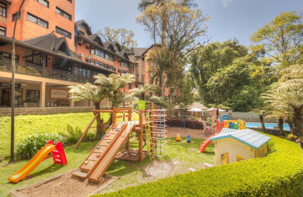 Parque infantil luminoso com escorregadores e estruturas de brincar num jardim ensolarado ao lado de um edifício.