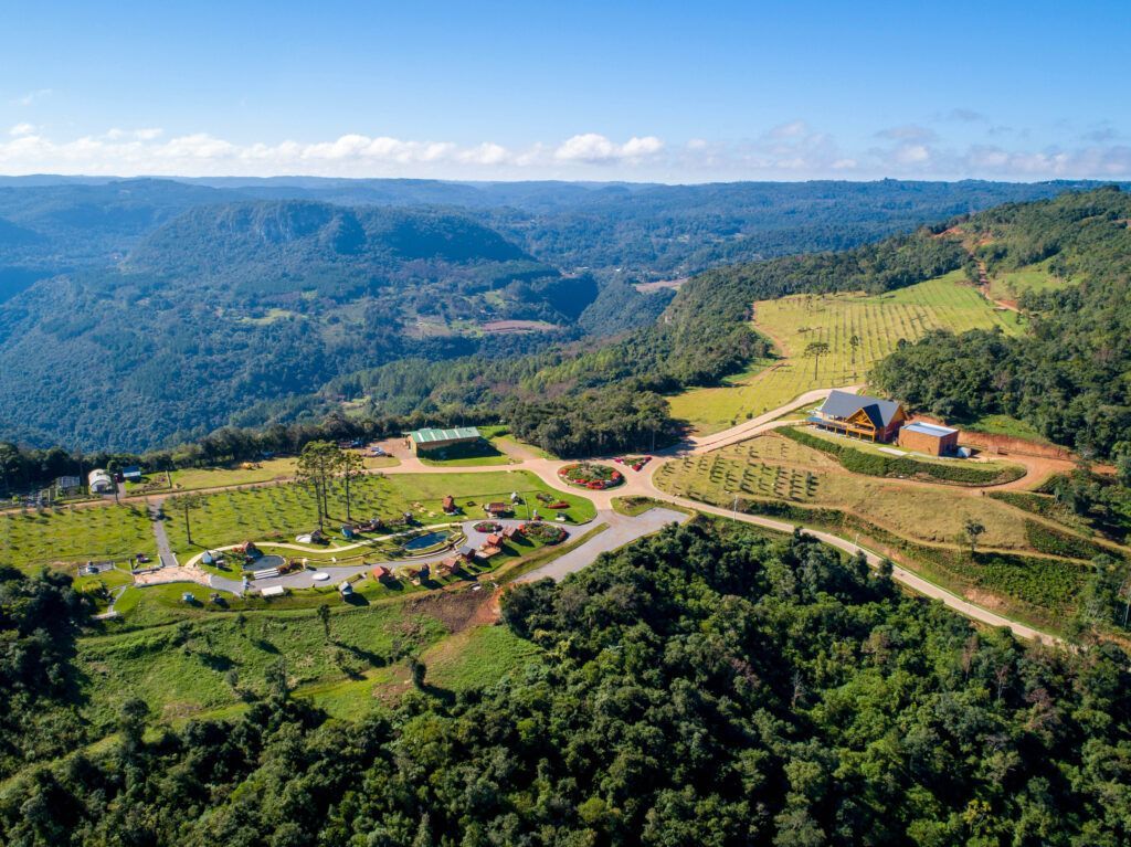 Vista panorâmica de colinas verdes, floresta e uma pequena vila sob um céu azul.