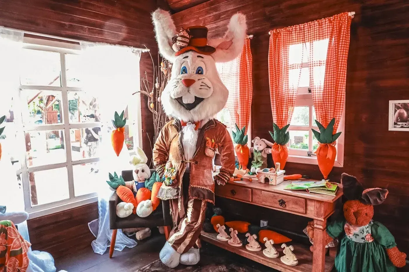 Sala festiva com uma grande estátua de mascote de coelho, decorações de cenoura e decoração aconchegante em madeira.