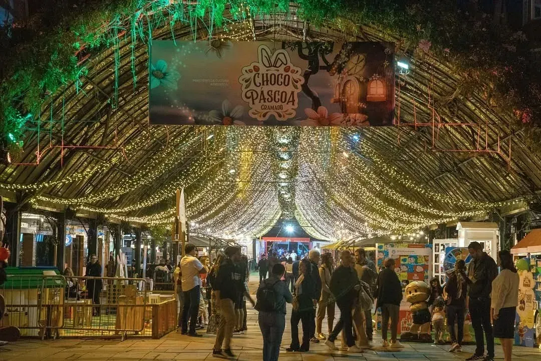 Mercado movimentado sob luzes coloridas e um toldo festivo à noite.