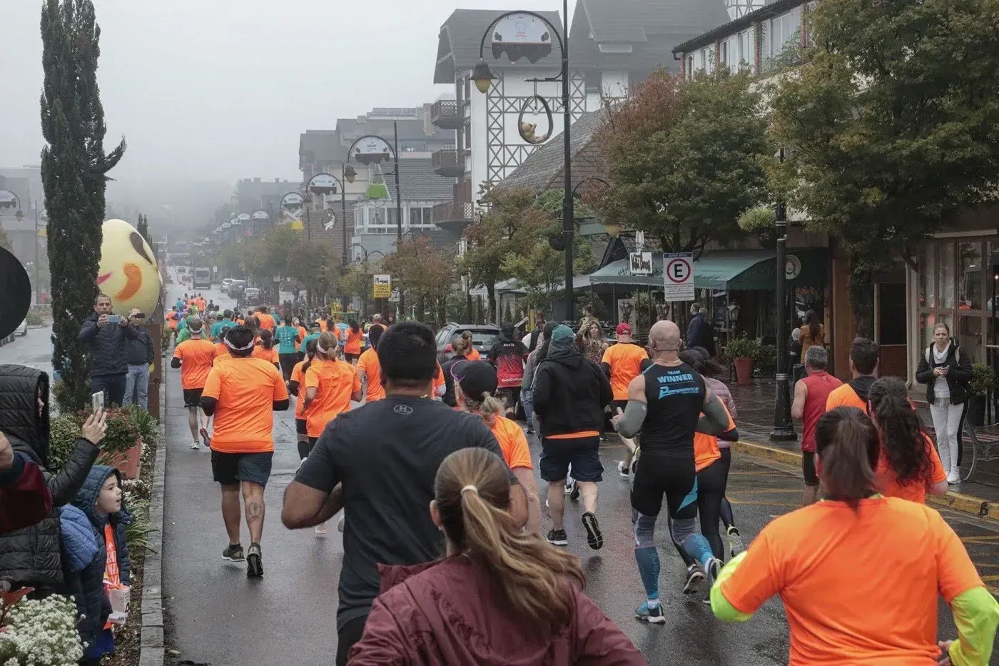 Corredores com camisetas laranjas ocupam uma rua molhada durante uma corrida ao ar livre em meio à neblina.
