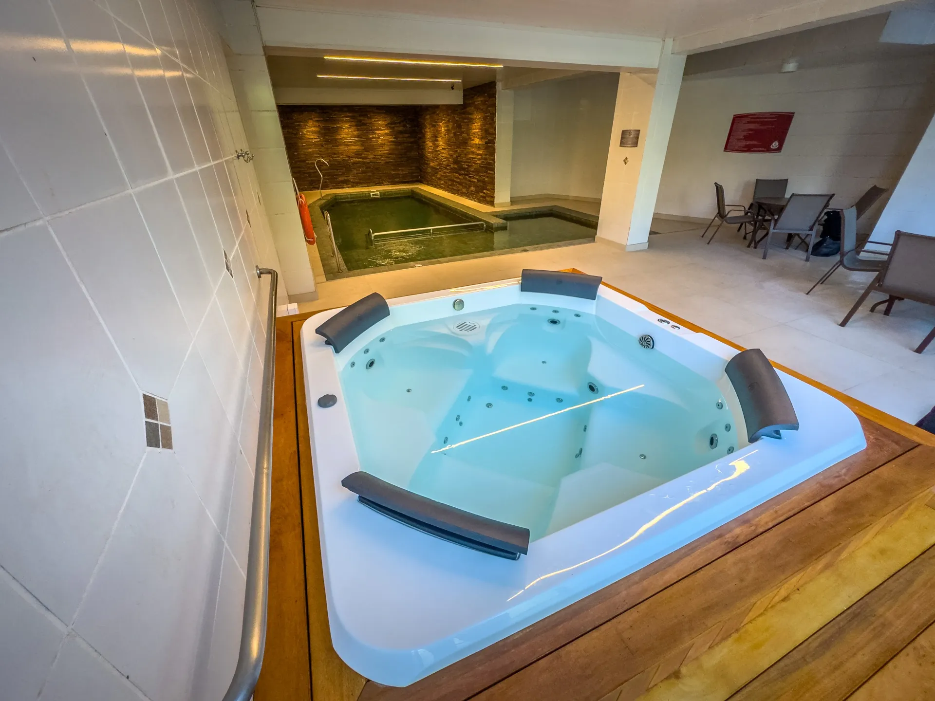 Banheira de hidromassagem com acabamento em madeira ao lado da piscina coberta e aquecida do Hotel Recanto da Serra.