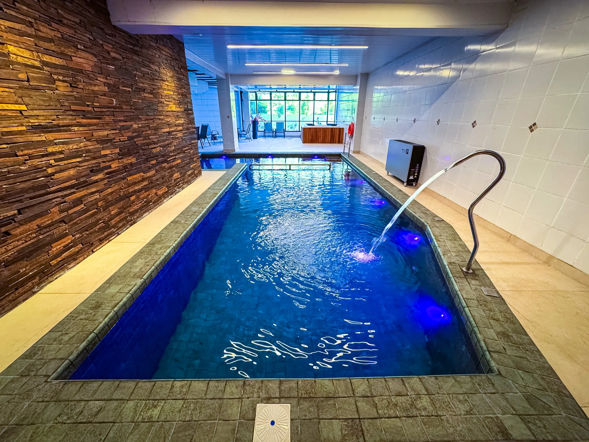 Coquetéis coloridos à beira da piscina em um dia ensolarado, com espreguiçadeiras e árvores ao fundo.