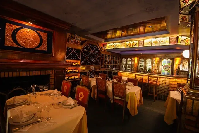 Ambiente interior acolhedor e sofisticado de um restaurante francês em Gramado, com mesas postas com toalhas brancas e amarelas e cadeiras estofadas em veludo vermelho.