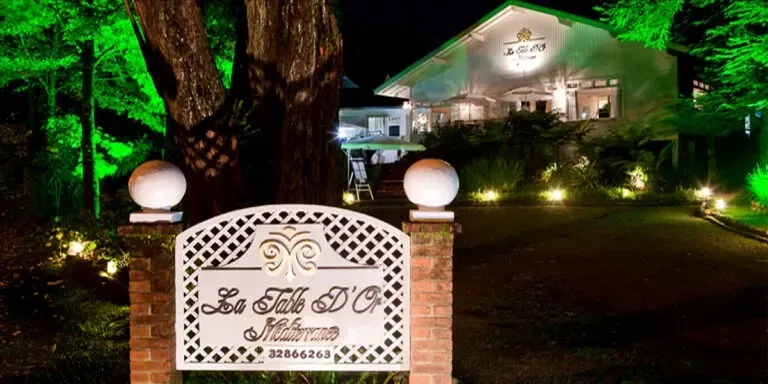 Fachada noturna do renomado restaurante francês La Table D'Or, em Gramado. A foto, tirada à noite, destaca a entrada em tijolos e ferro forjado com o nome do restaurante e o letreiro 