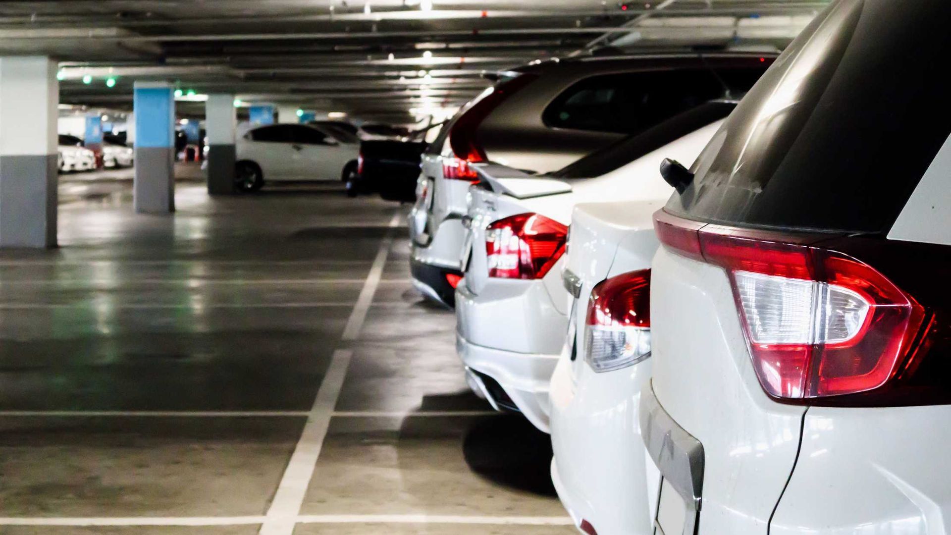 Row of parked cars in an underground parking garage, shown from the rear side.