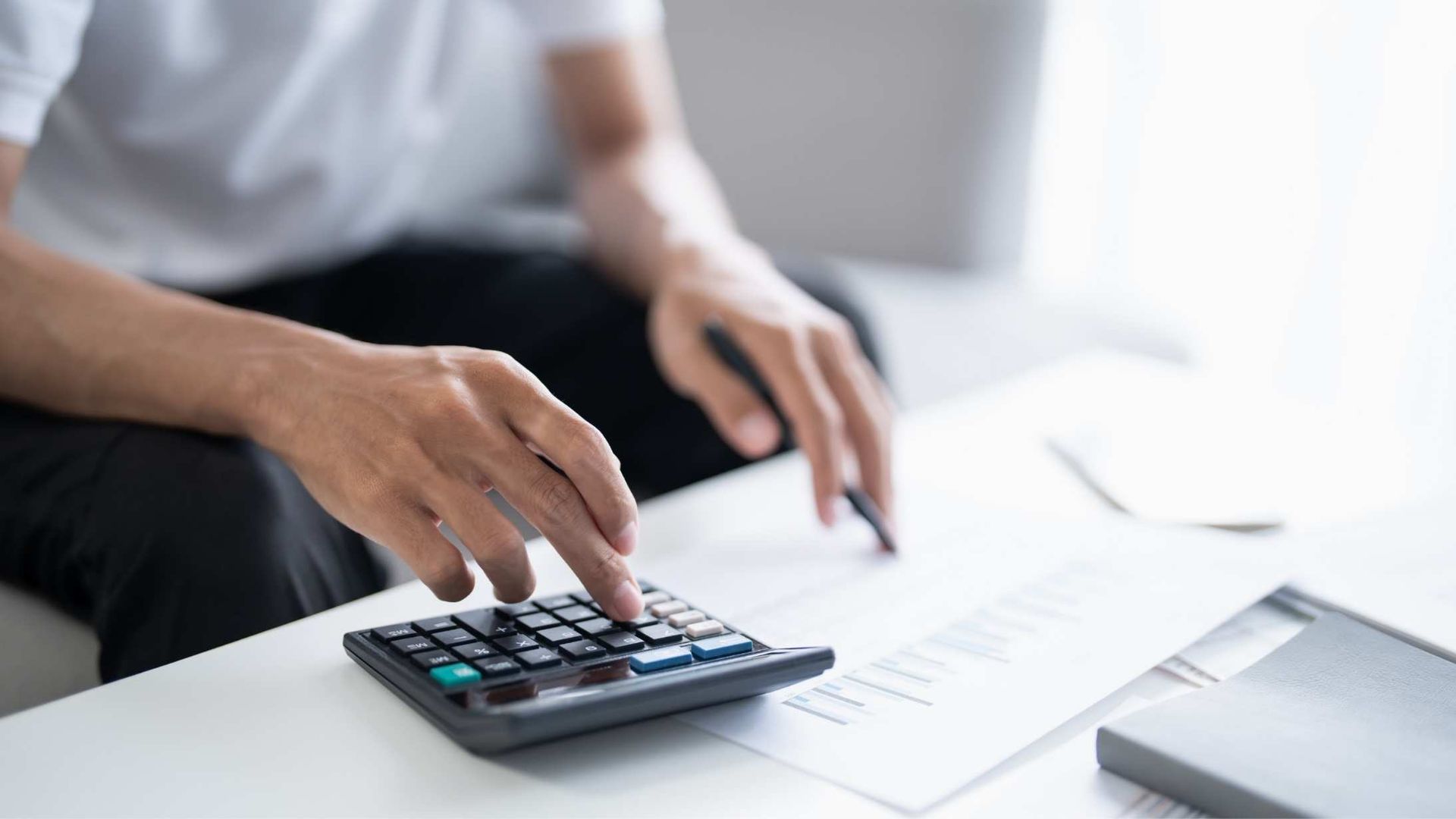 Hands using a calculator beside financial papers on a desk