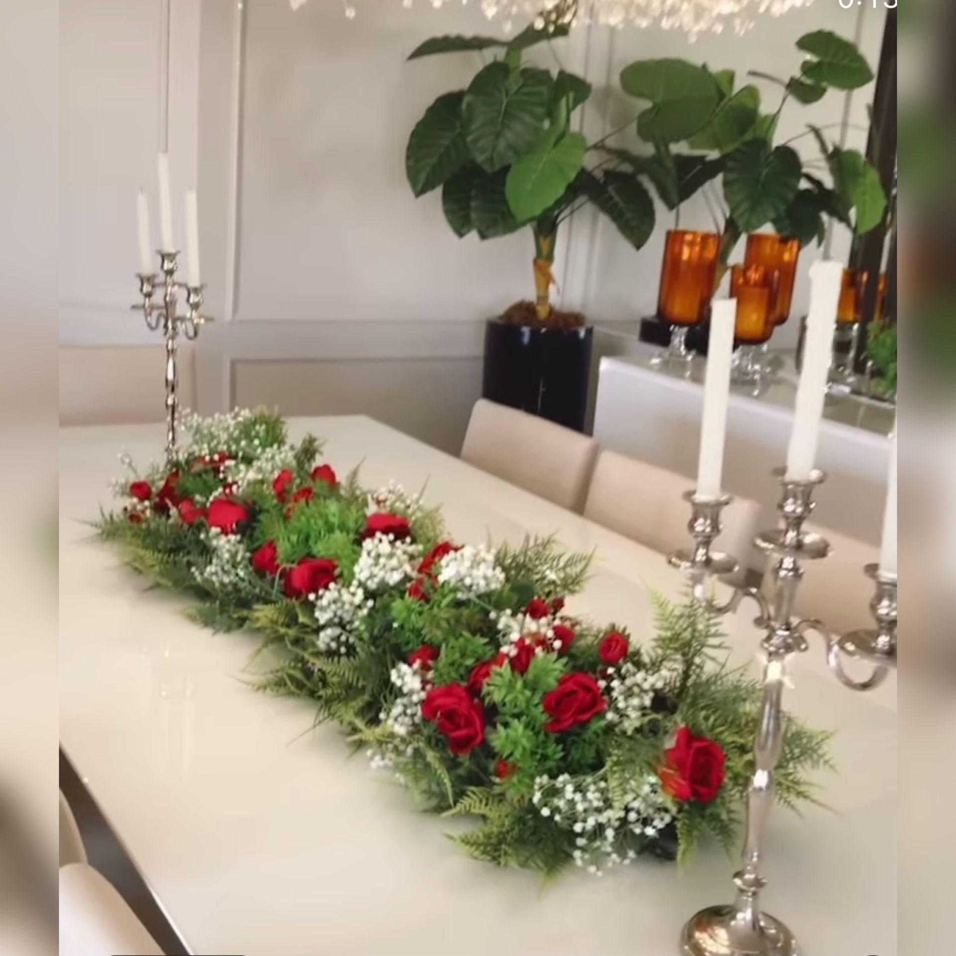 Dining table with a floral centerpiece, surrounded by candelabras and a large potted plant.