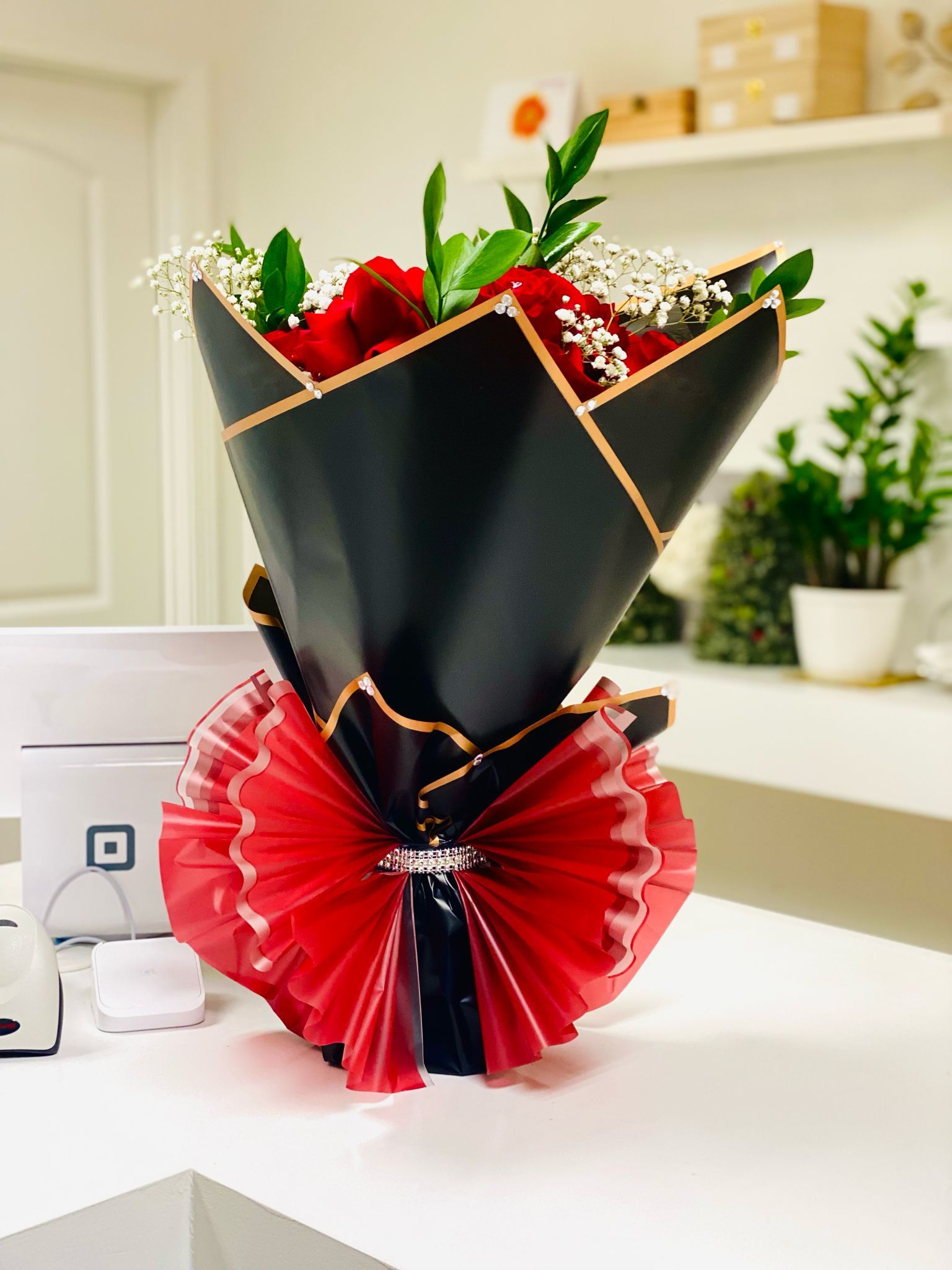 Luxury & premium Bouquet of red roses wrapped in black paper and red ribbon, on a white counter.