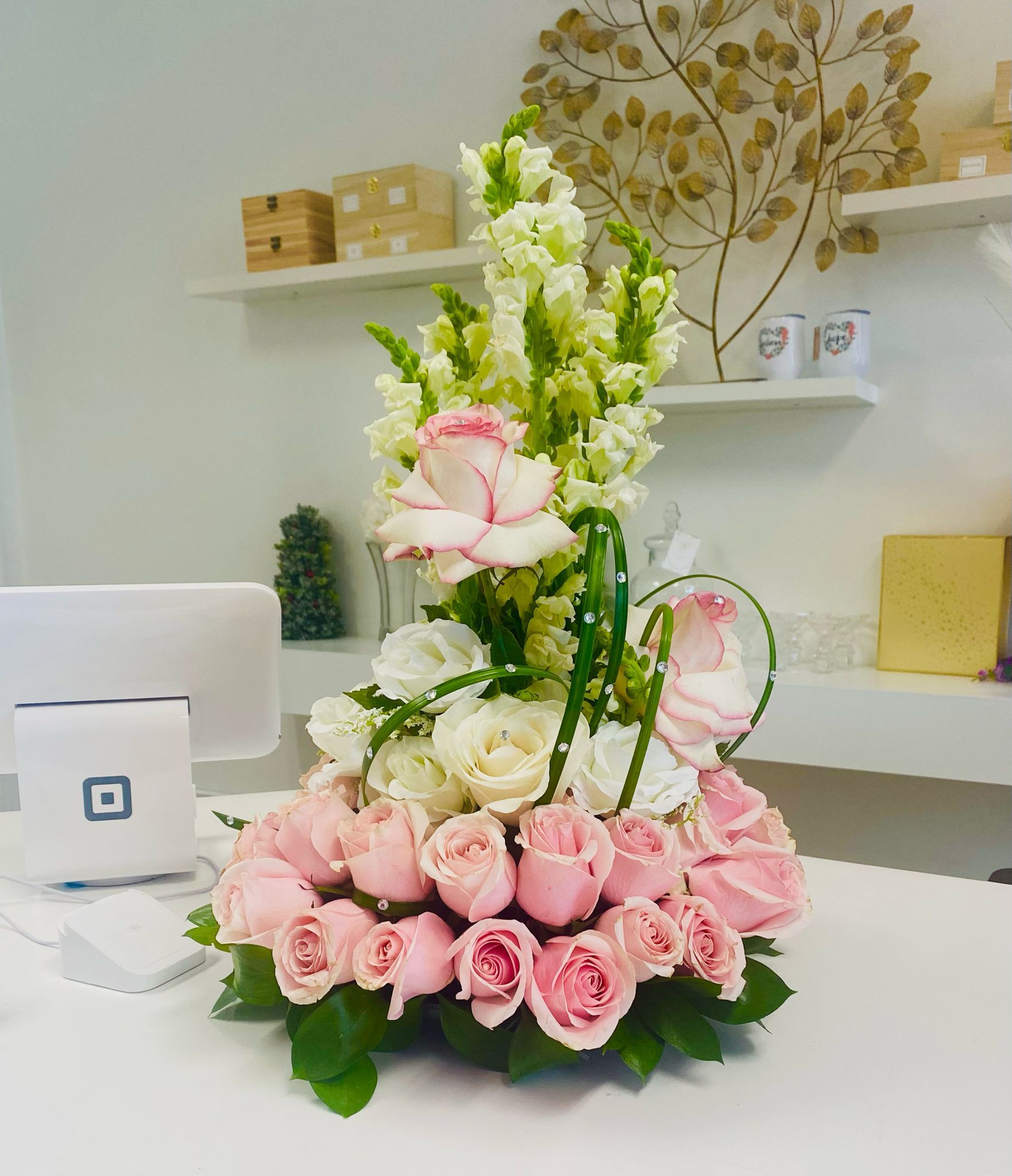 Premium Floral arrangement with pink roses, white roses, and green snapdragons on a counter.