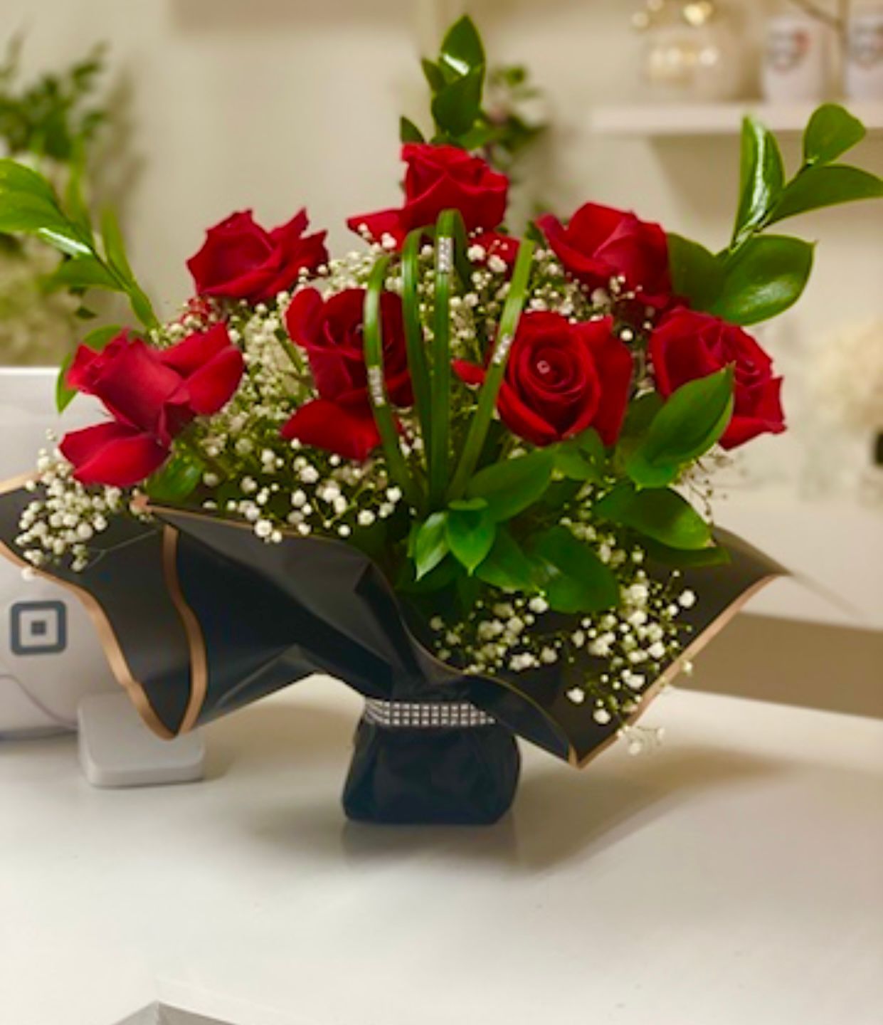 Luxury & premium Red roses and baby's breath floral arrangement in a black vase with green leaves and gold trim.