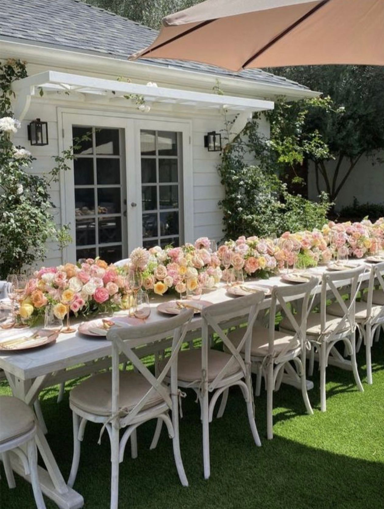 Outdoor dining table set for a party, decorated with flowers on a grassy lawn.