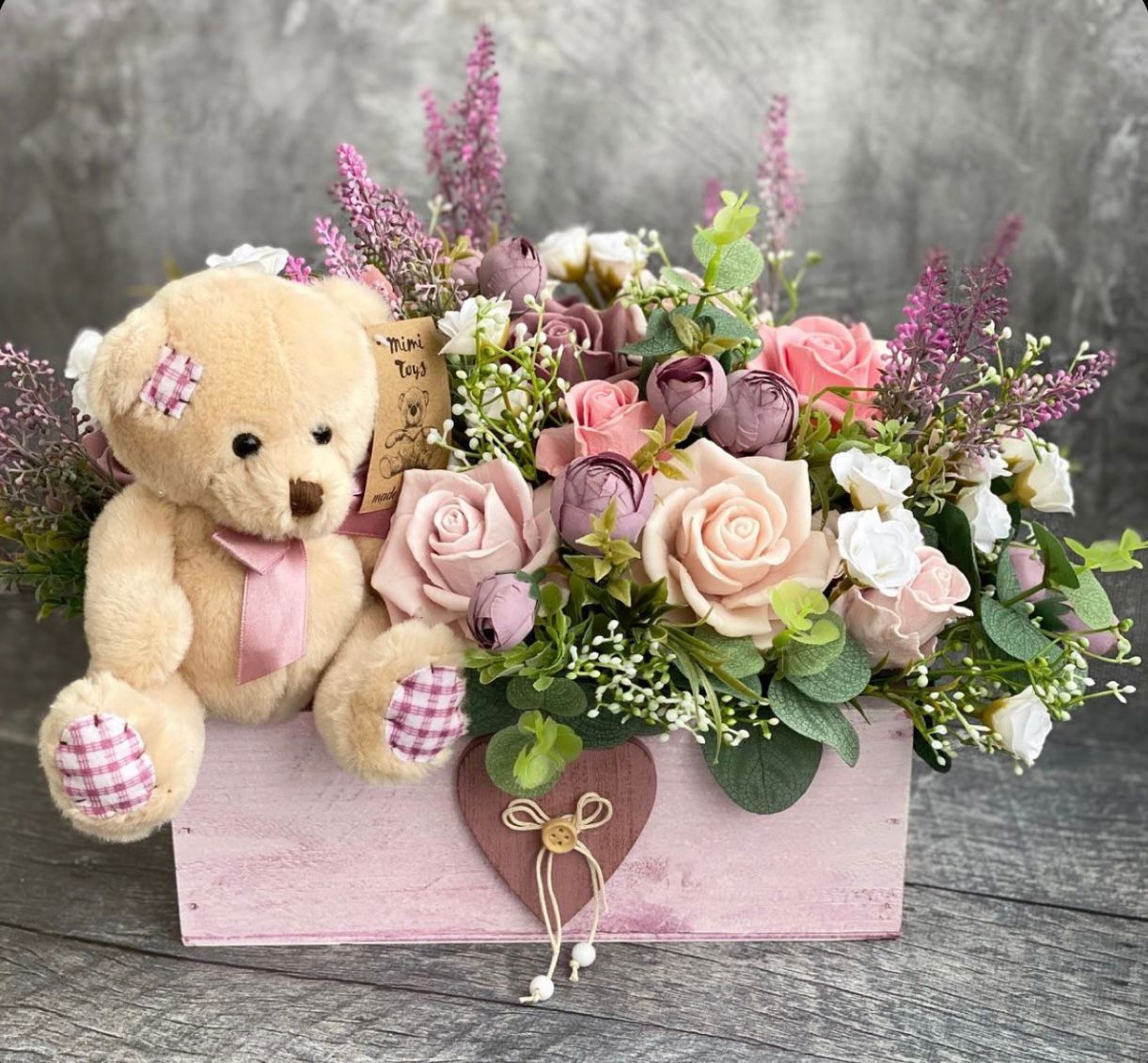 Teddy bear with pink flowers in a pink wooden box.