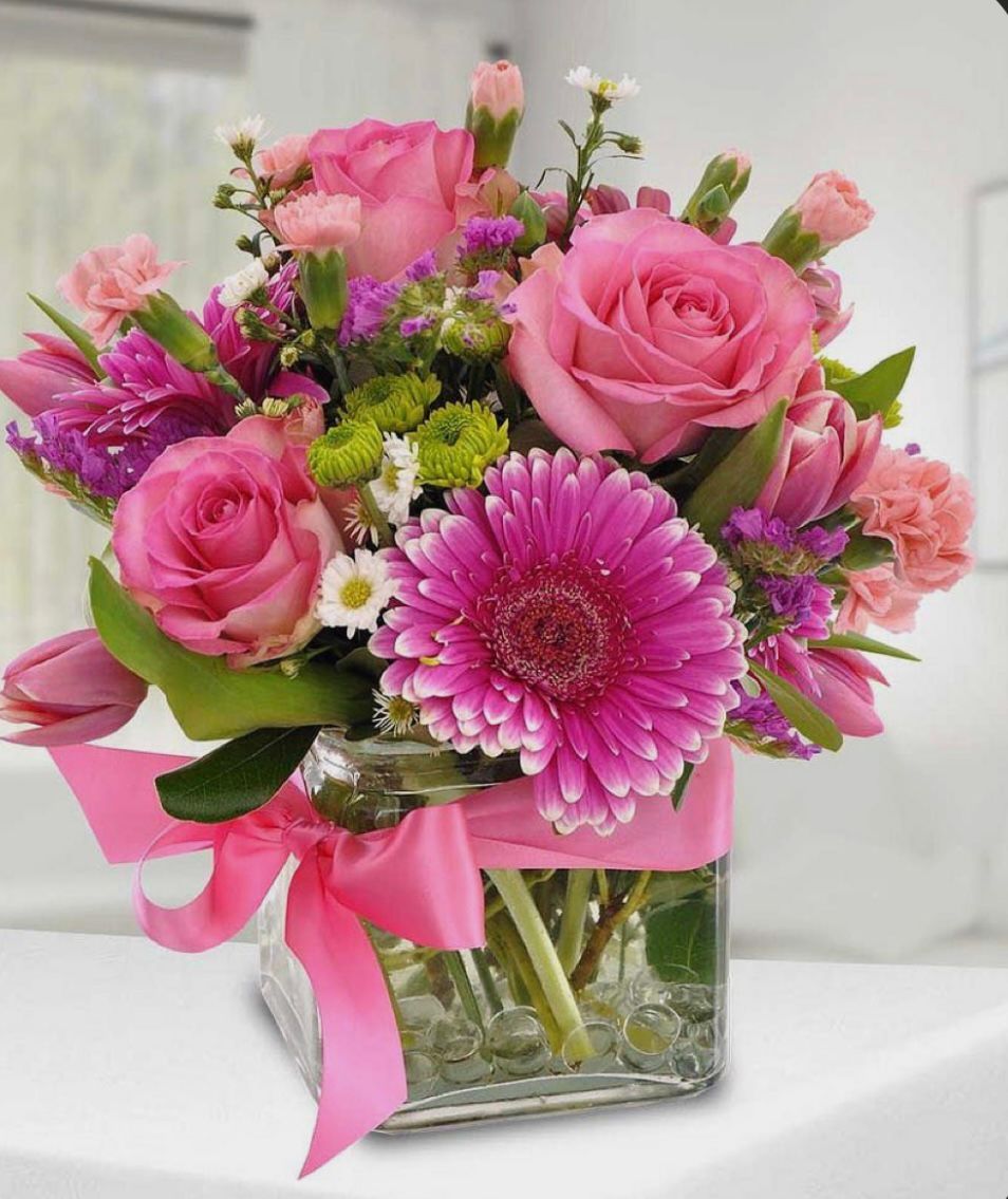 Pink and purple flower arrangement in a square glass vase tied with a pink ribbon.