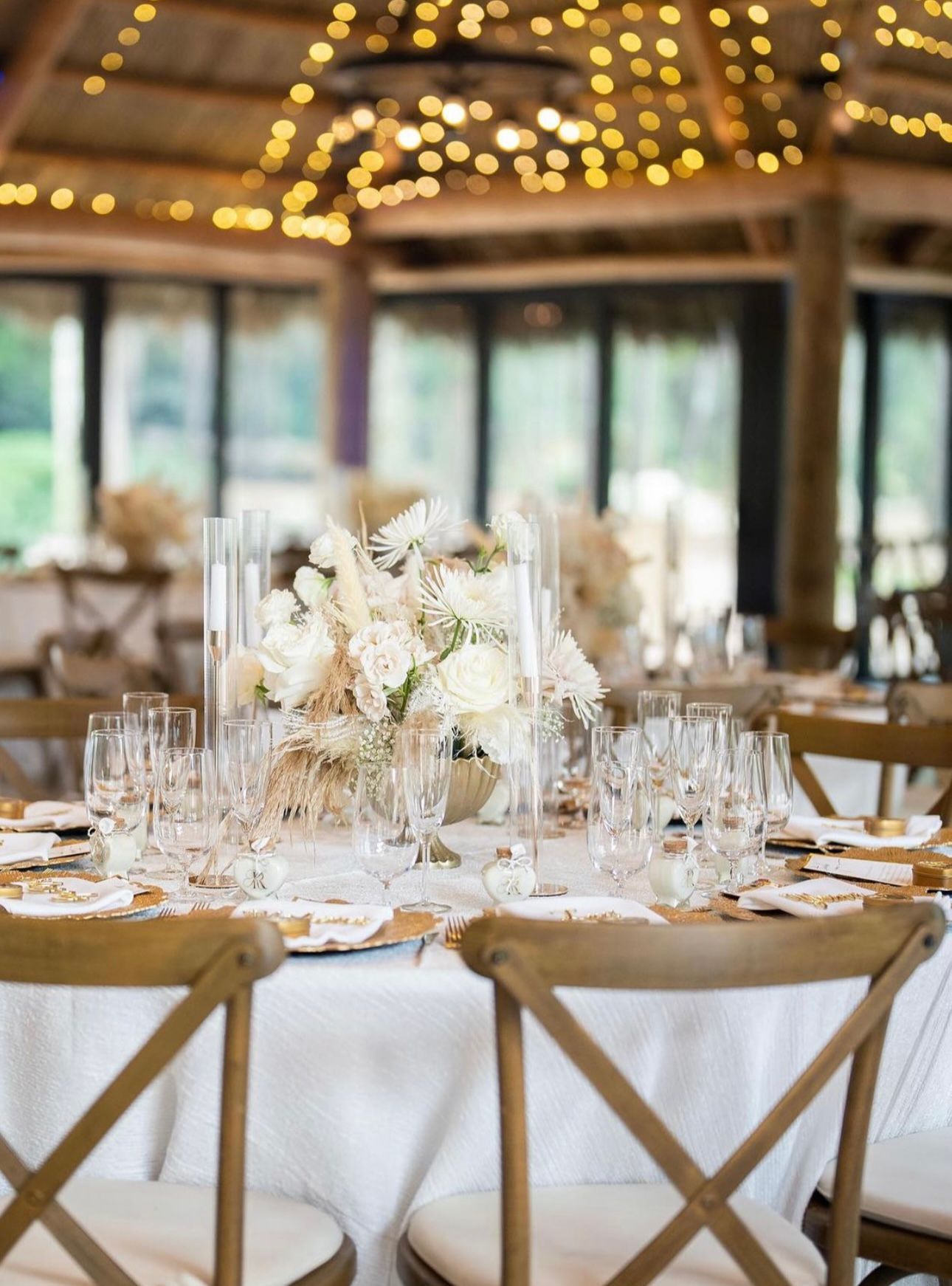 Elegant wedding table setting with floral centerpiece, clear glasses, and wooden chairs.