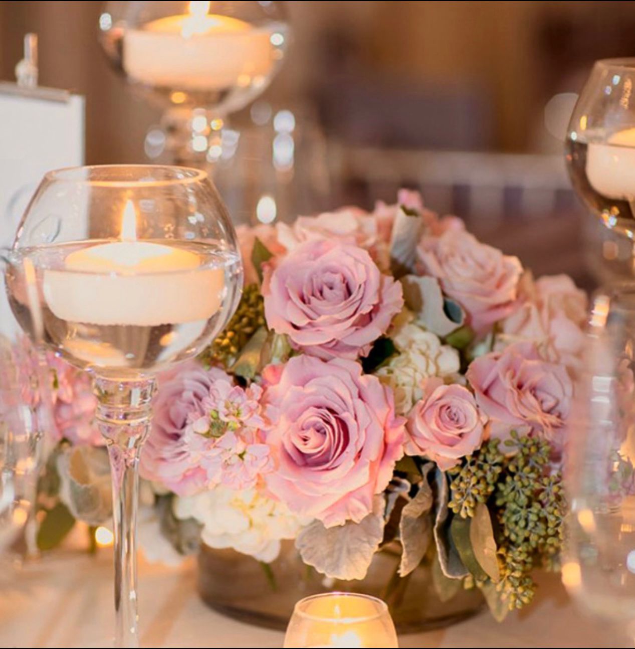 Floral centerpiece of pink roses with floating candles in glass.