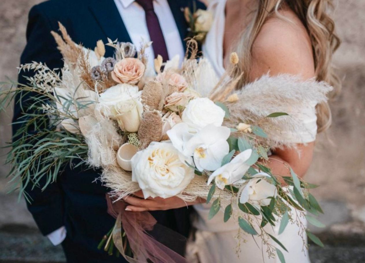 Bride and groom holding a bouquet of white and beige flowers with pampas grass.
