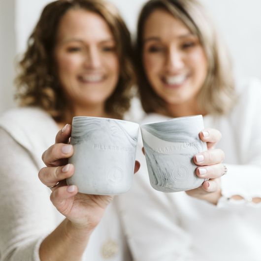Two people holding up matching white cups and smiling in a bright setting