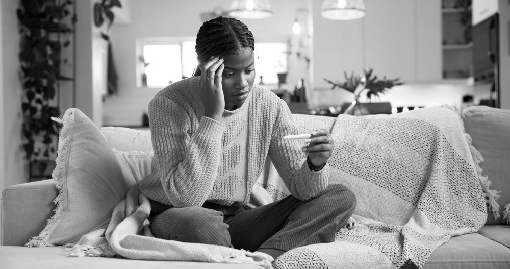 Person sitting on a couch, looking at a pregnancy test in a living room.
