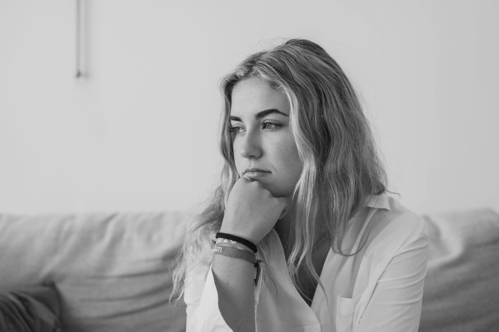 Person sitting on a couch, resting chin on hand, looking pensive in a black-and-white scene.