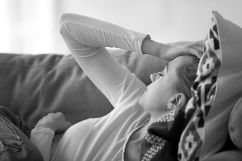 Tired woman lying on a couch with her hand on her forehead, appearing unwell or fatigued.