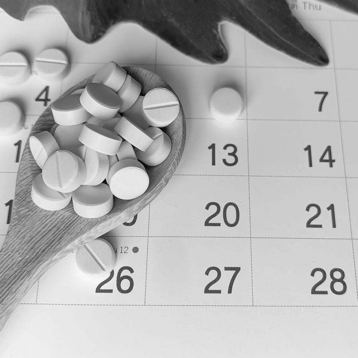 White pills on a wooden spoon placed over a calendar, symbolizing medication or menstrual tracking.