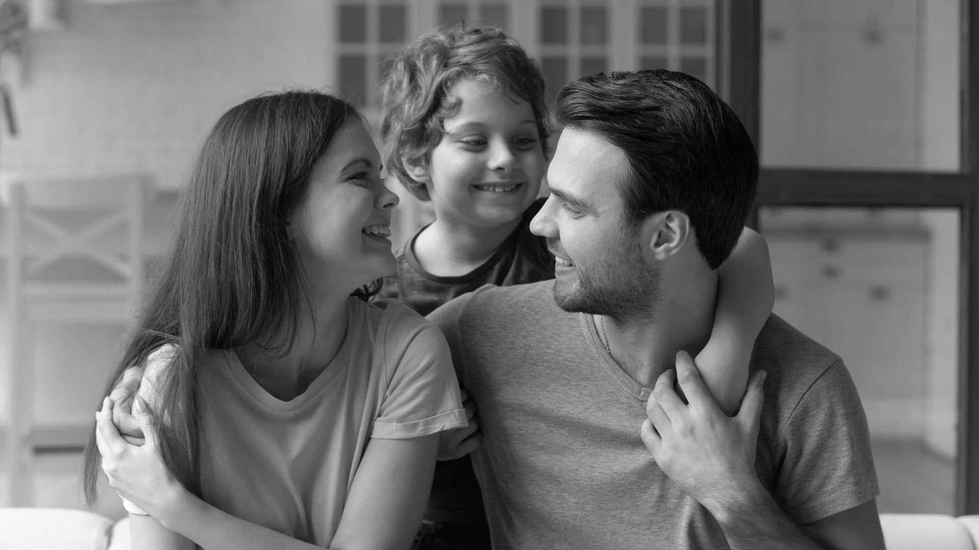 Happy family sitting together at home, smiling and looking at each other with warmth and connection.