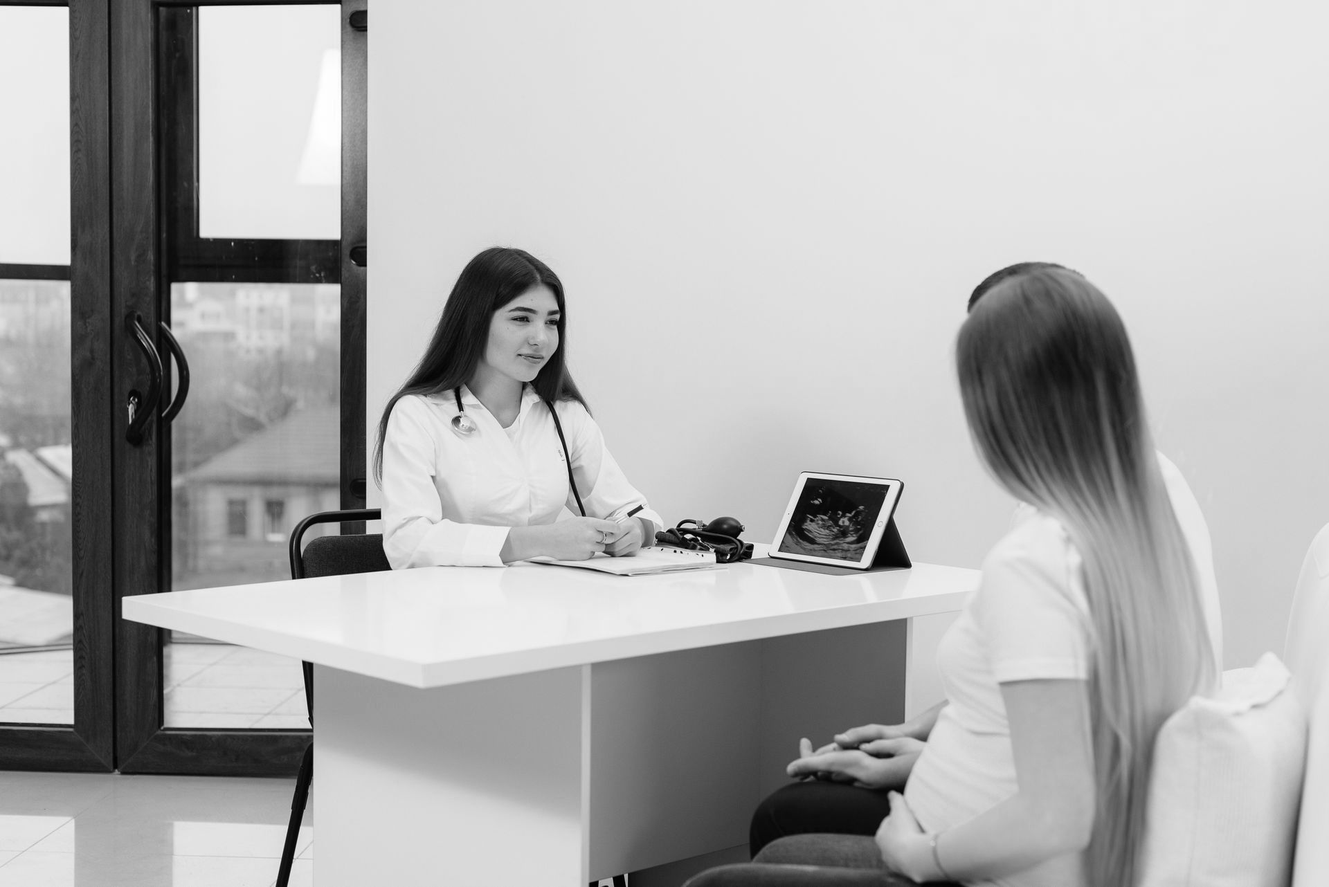 Healthcare professional meeting with pregnant woman and partner, discussing ultrasound results.