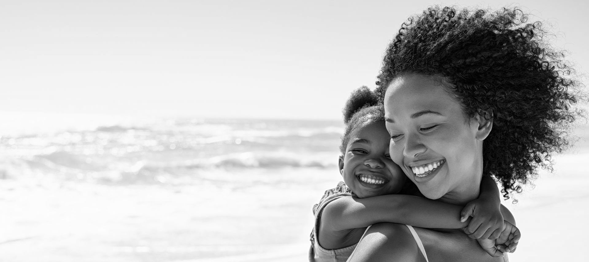 Smiling mother holding her happy child on a sunny beach, both laughing and enjoying time together.
