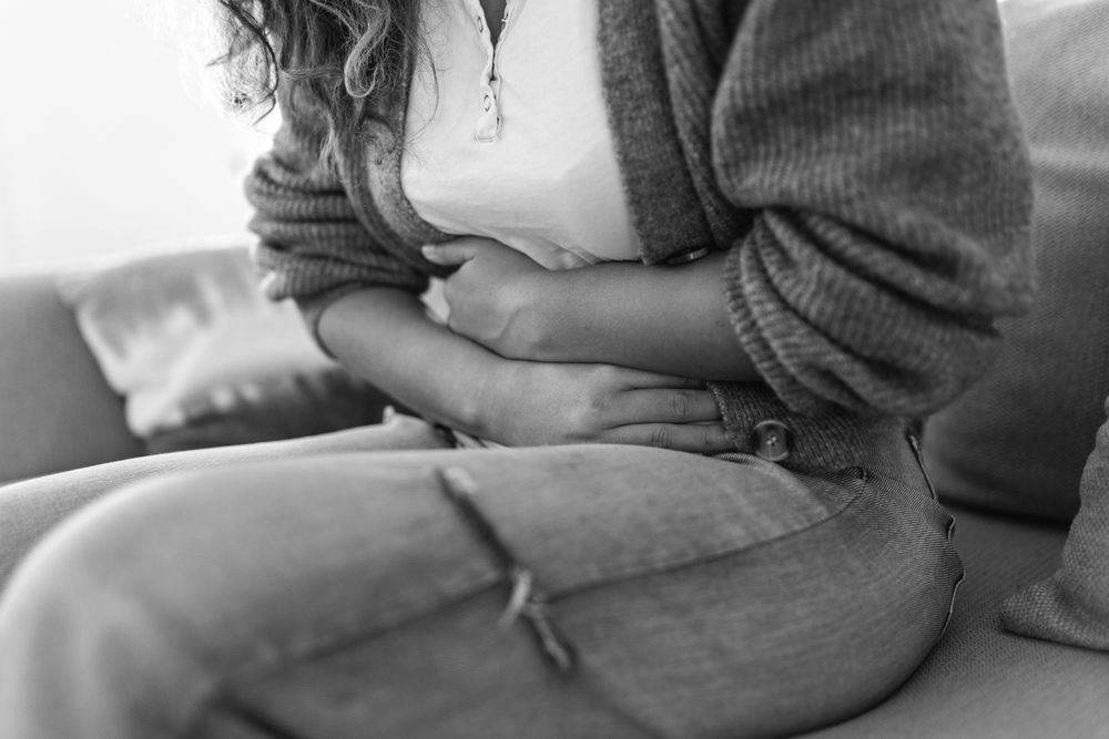 A woman is sitting on a couch holding her stomach in pain.