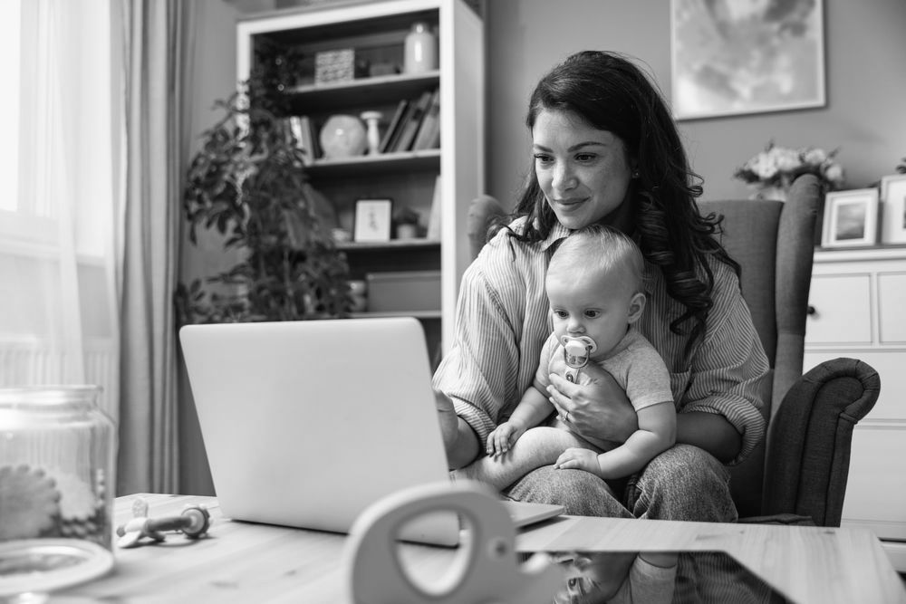 A woman is holding a baby while using a laptop computer.
