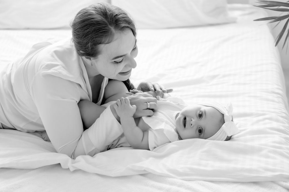 A woman is laying on a bed with a baby wrapped in a blanket.