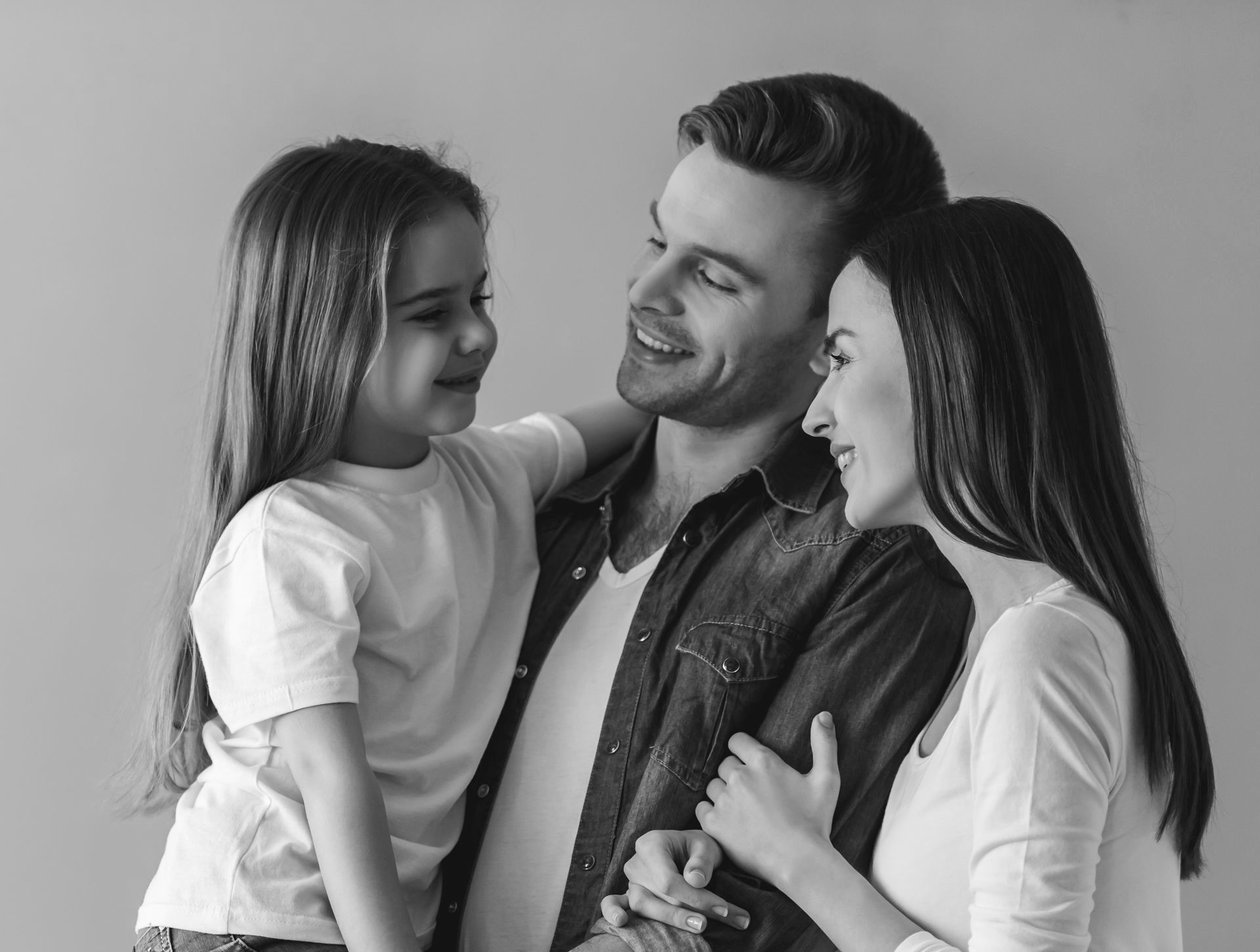 Smiling family of three standing together, with parents embracing their young daughter affectionately.