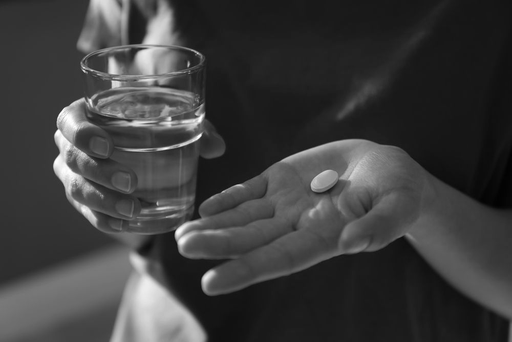 Hand holding a glass of water while another hand holds a white pill over an open palm