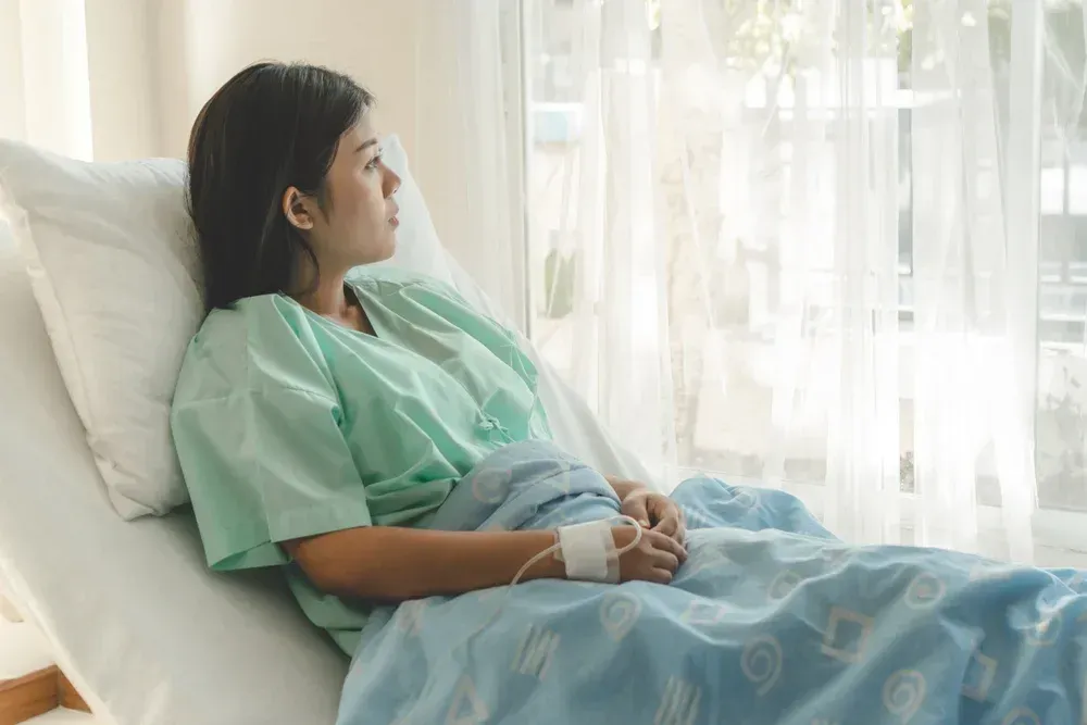 A woman is laying in a hospital bed looking out the window.