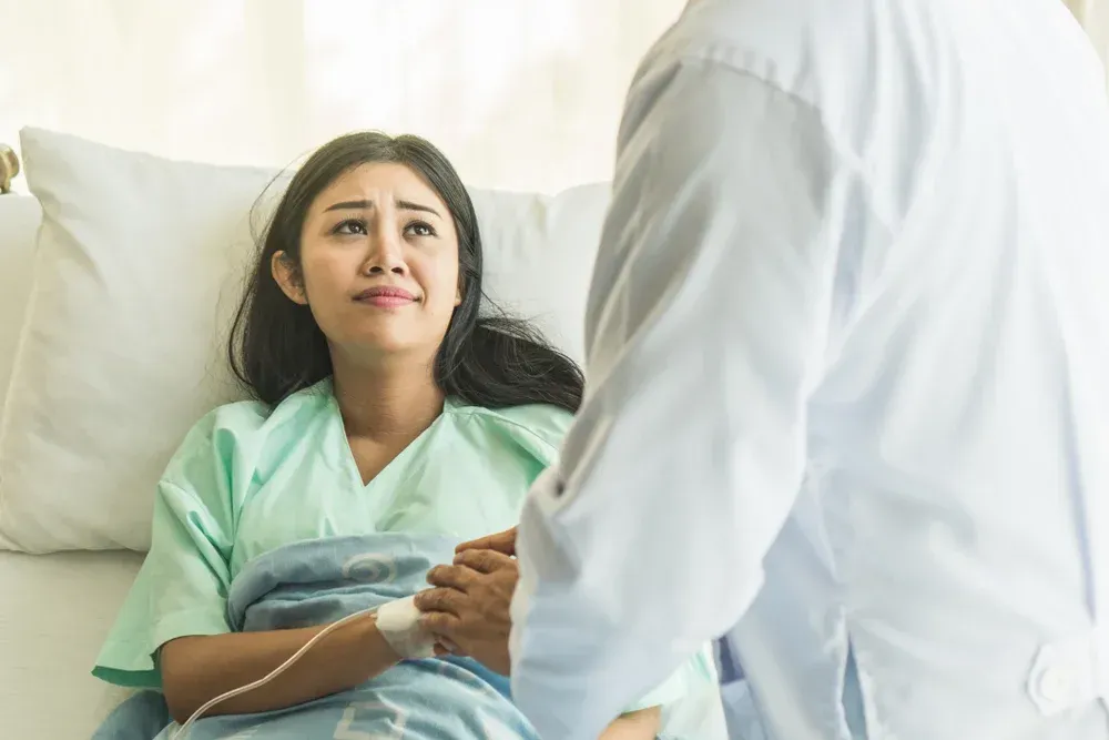 A woman is laying in a hospital bed talking to a doctor.