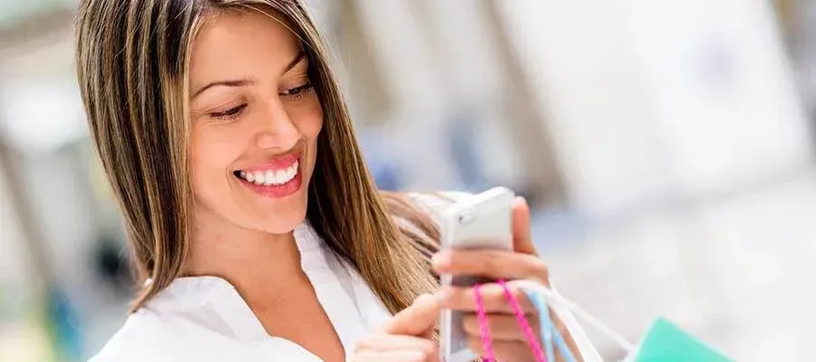 A woman is holding shopping bags and looking at her cell phone.