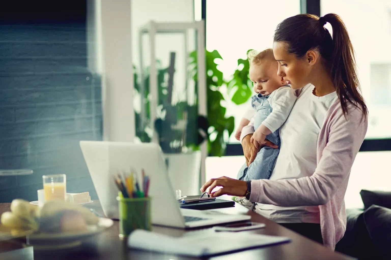 A woman is holding a baby while using a laptop computer.