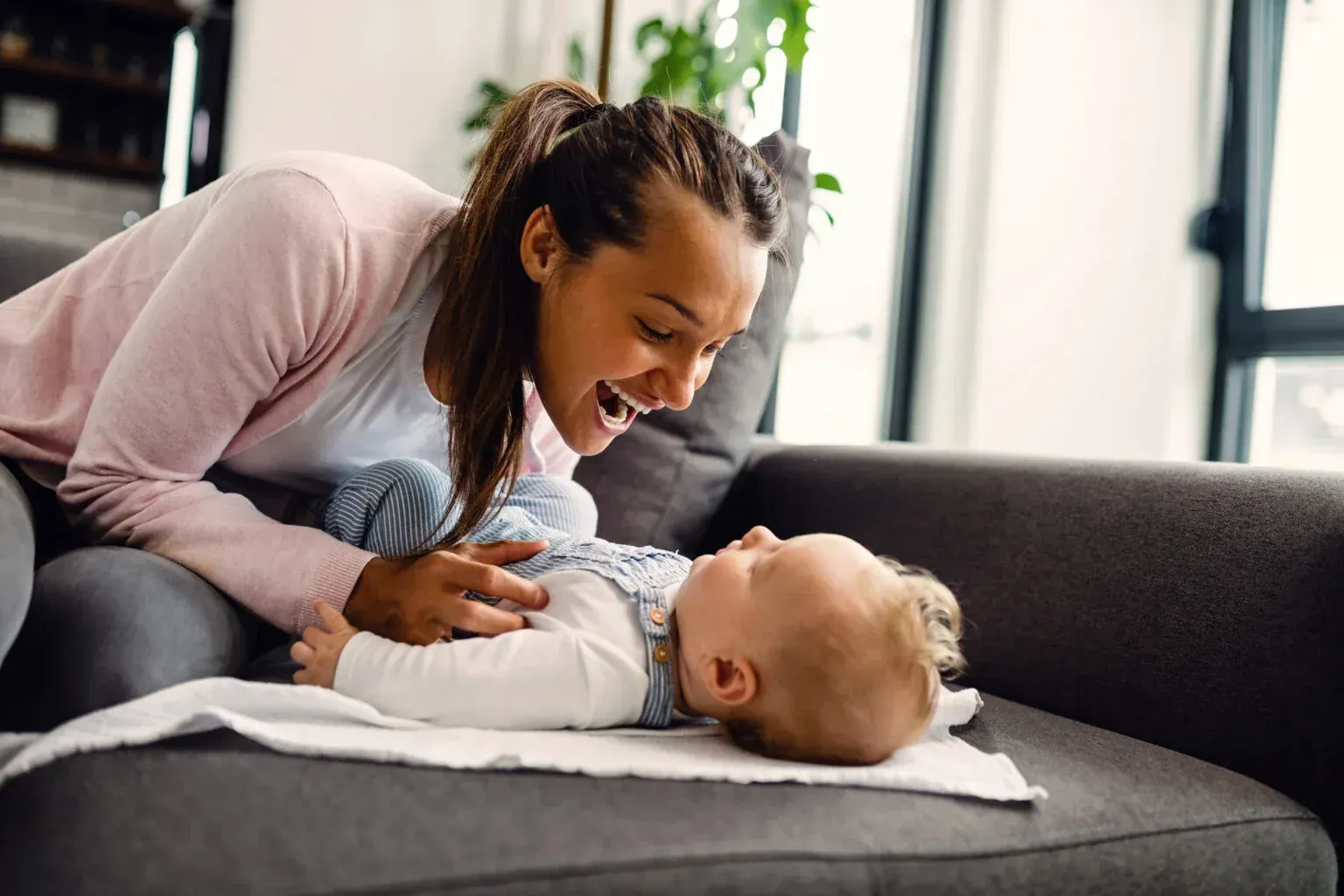 Mother smiling and bonding with her baby on the couch, representing postpartum depression self-care and emotional healing.
