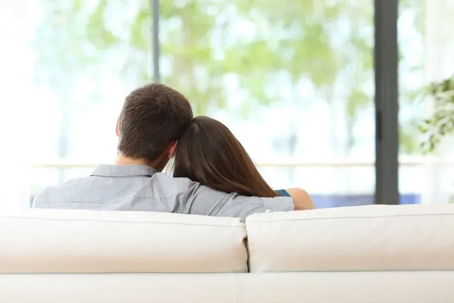 A man and a woman are sitting on a couch looking out a window.