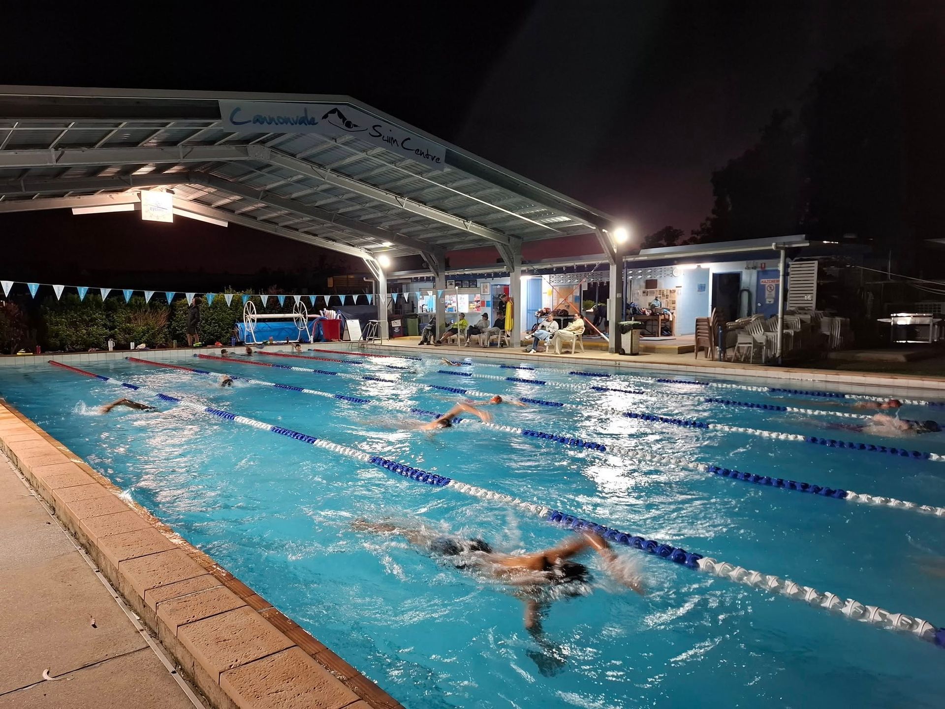 Swimmers in Lanes at an Outdoor Pool Under a Metal Canopy at Night — Cannonvale Swim Centre In Cannonvale, QLD
