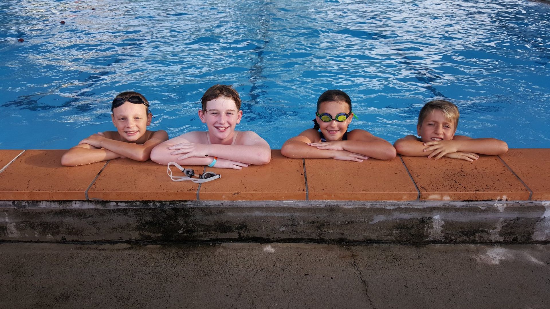 Four People Rest Their Arms on the Edge of a Swimming Pool — Cannonvale Swim Centre In Cannonvale, QLD