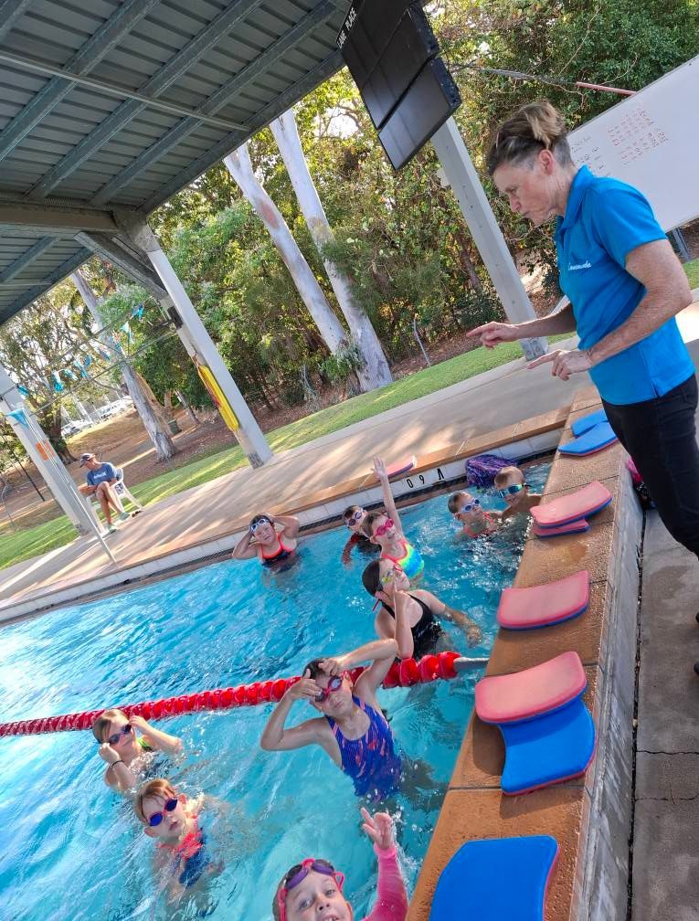 Swimming Instructor With Students In Pool, Some Holding Up Hands — Cannonvale Swim Centre In Cannonvale, QLD