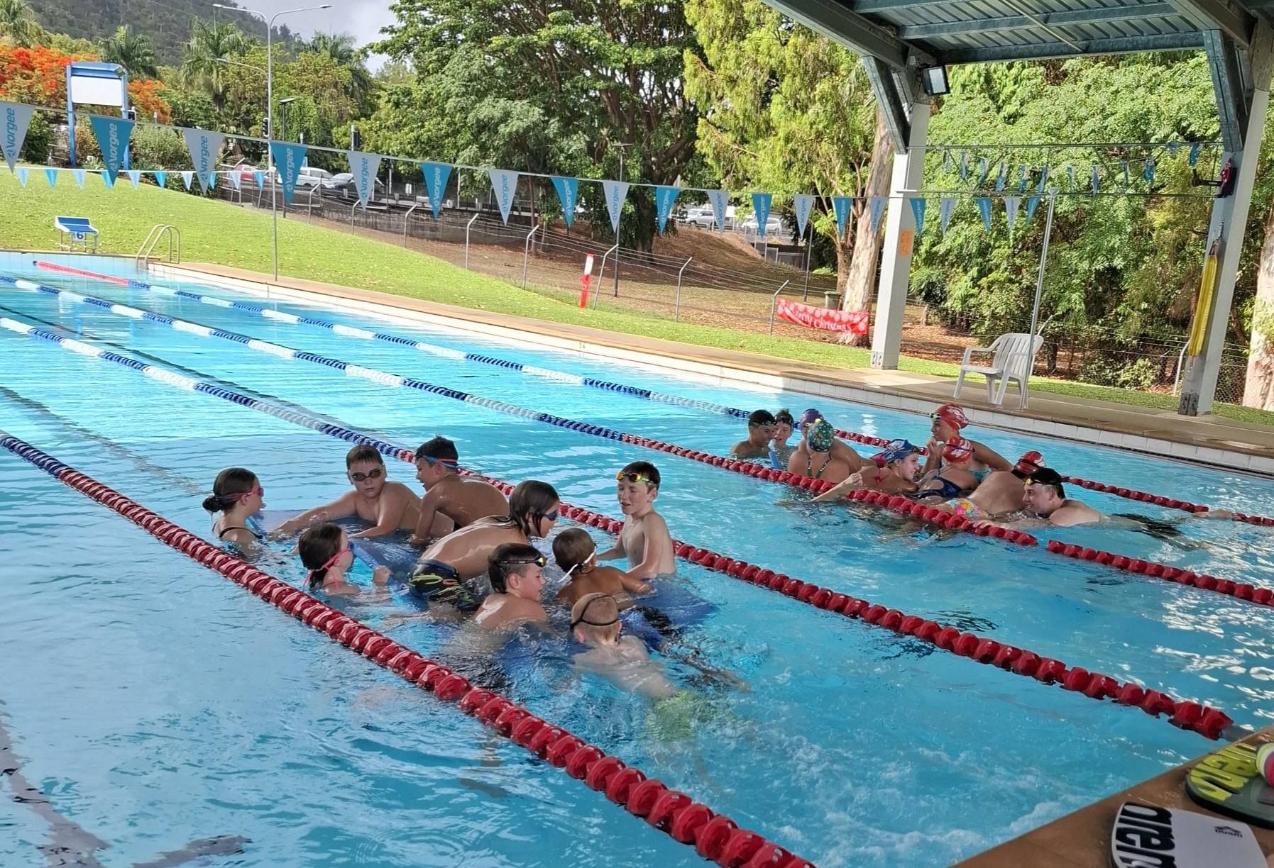 People Swimming In A Blue Outdoor Pool With Lane Markers, Under A Canopy — Cannonvale Swim Centre In Cannonvale, QLD